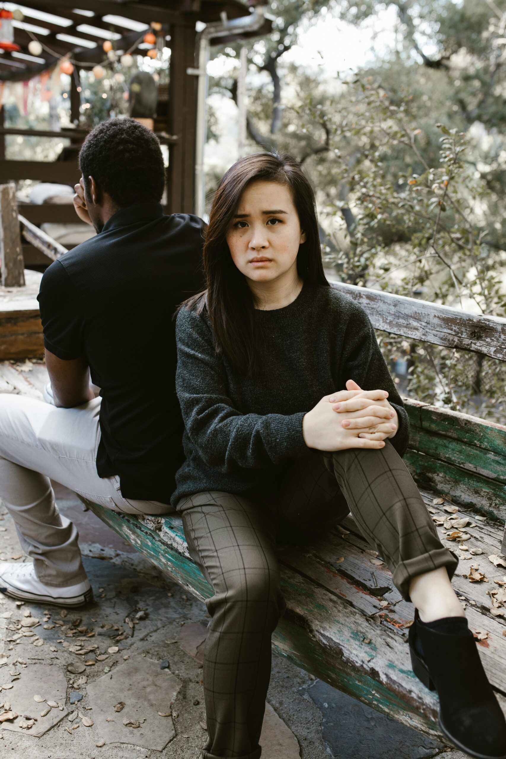 Couple sitting outdoors back to back, looking frustrated and angry at each other, representing emotional distance and conflict in relationships